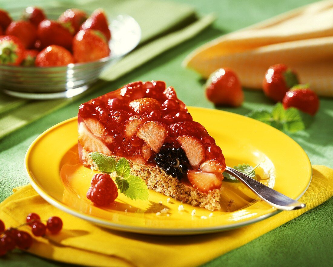 Stück Beerentorte auf gelbem Teller; frische Erdbeeren