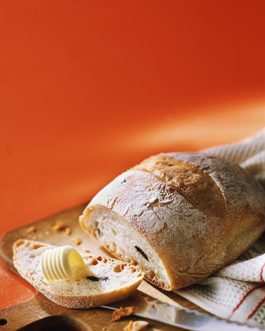 Olivenbrot mit abgeschnittener Scheibe und Butterröllchen