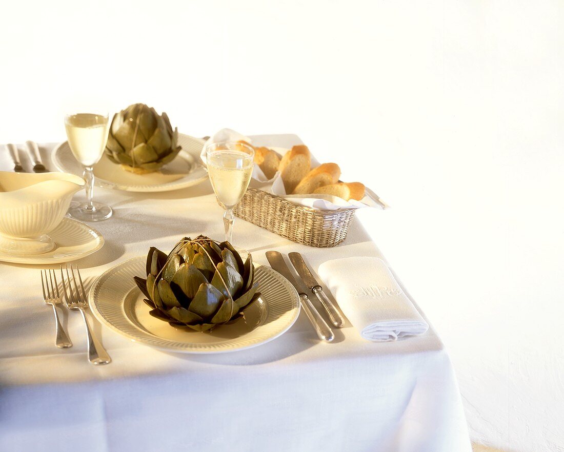 Artichokes, white wine and baguette on laid table