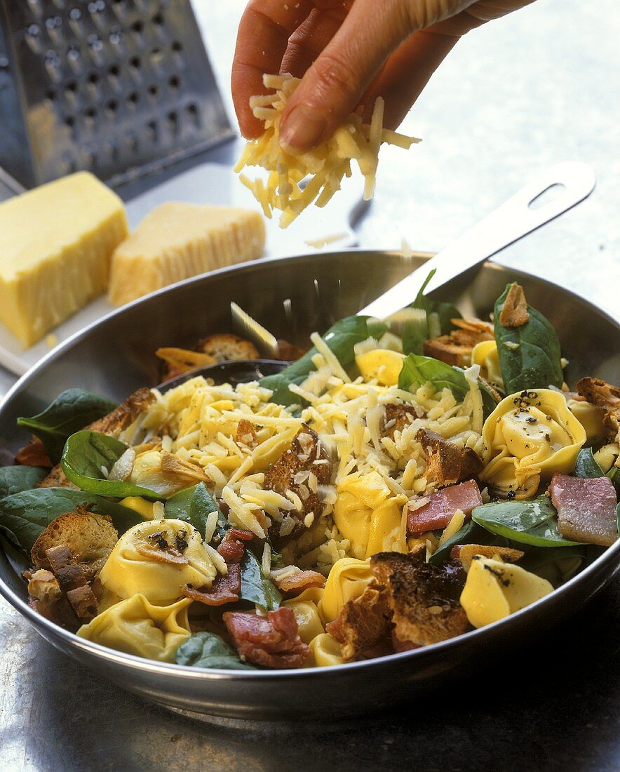 Hand streut Käse über Tortellini-Spinat-Pfanne
