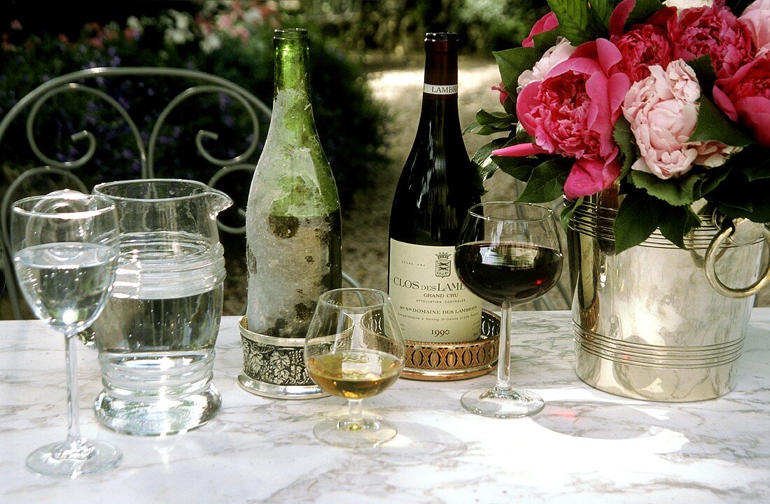 Wein, Cognac, Wasser und Pfingstrosen auf Tisch im Freien