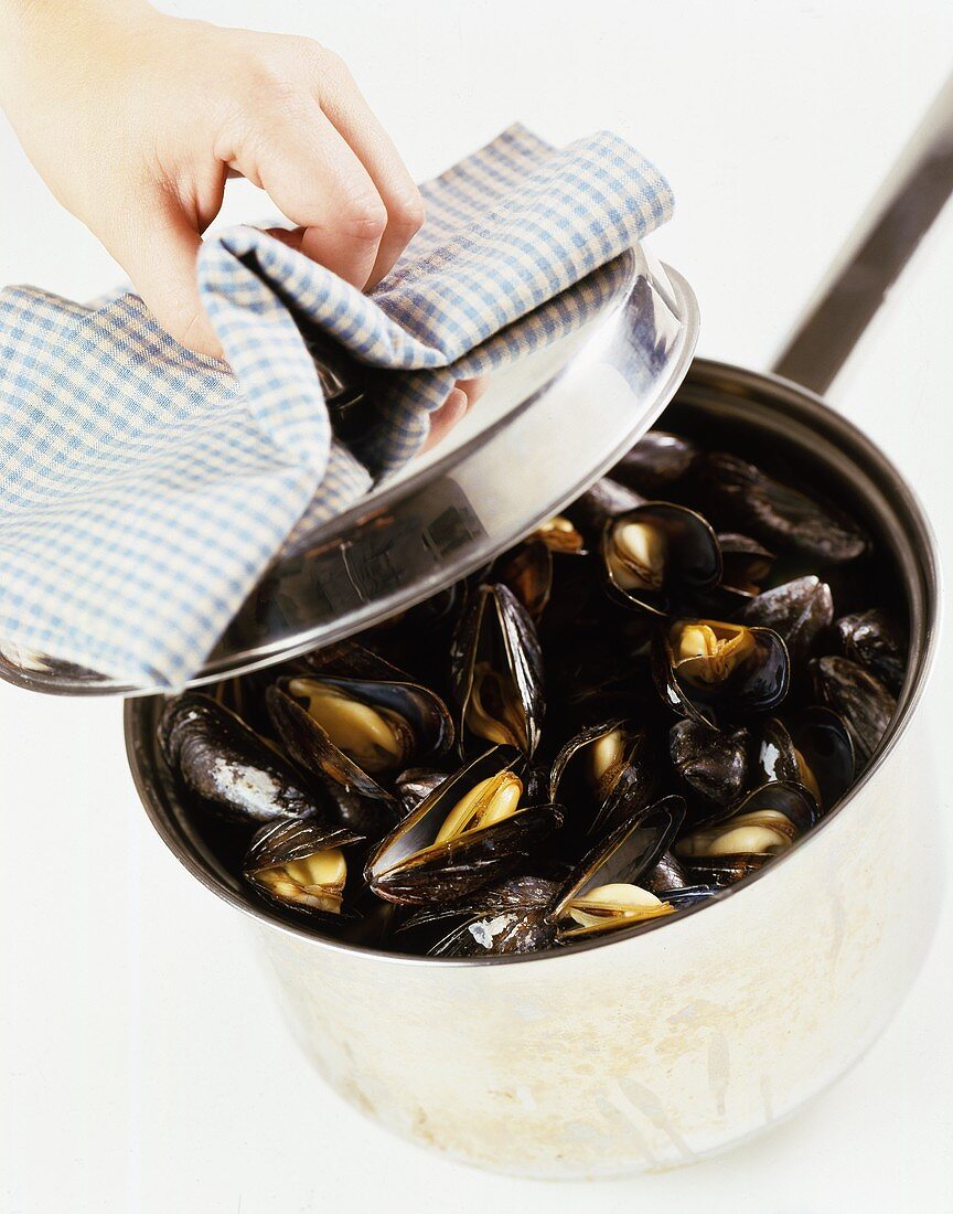 Hand lifting lid from pan of mussels
