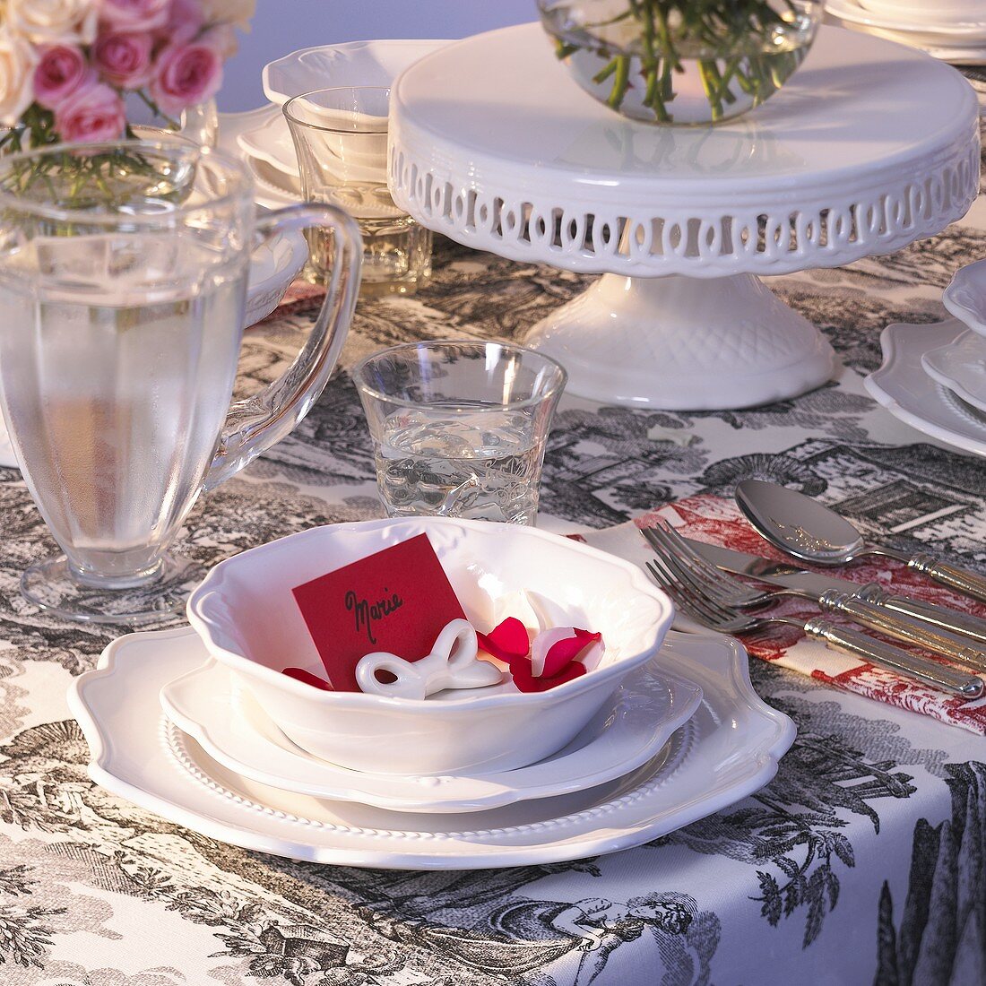 Festliches Gedeck mit weißem Geschirr und roter Tischkarte