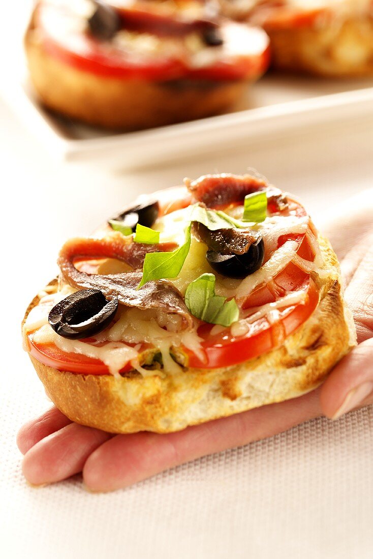 Hand holding mini-pizza with tomatoes, olives and anchovies