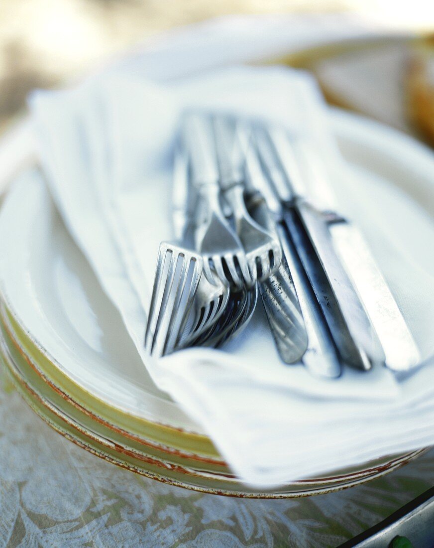 Knives and forks on napkin on pile of plates