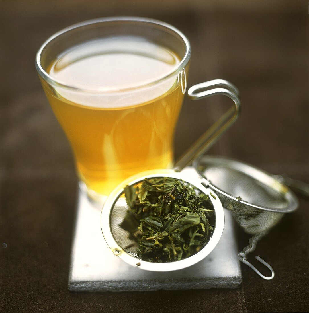 Grüner Tee in Glastasse und Teeblätter im Sieb