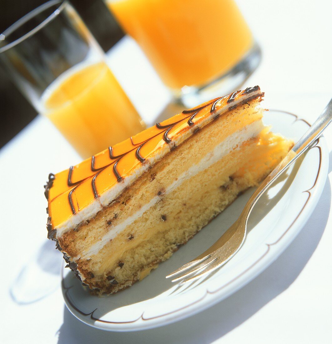 Piece of rum gateau and orange juice on table