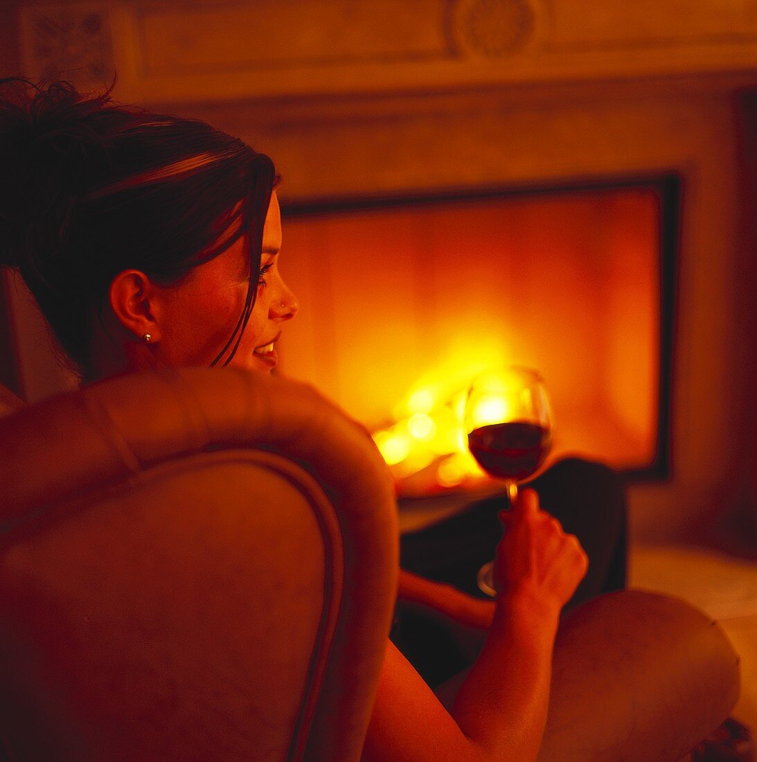 Junge Frau mit Glas Rotwein am Kaminfeuer