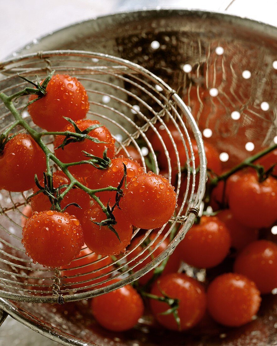 Cherry tomatoes with drops of water in strainer and on server