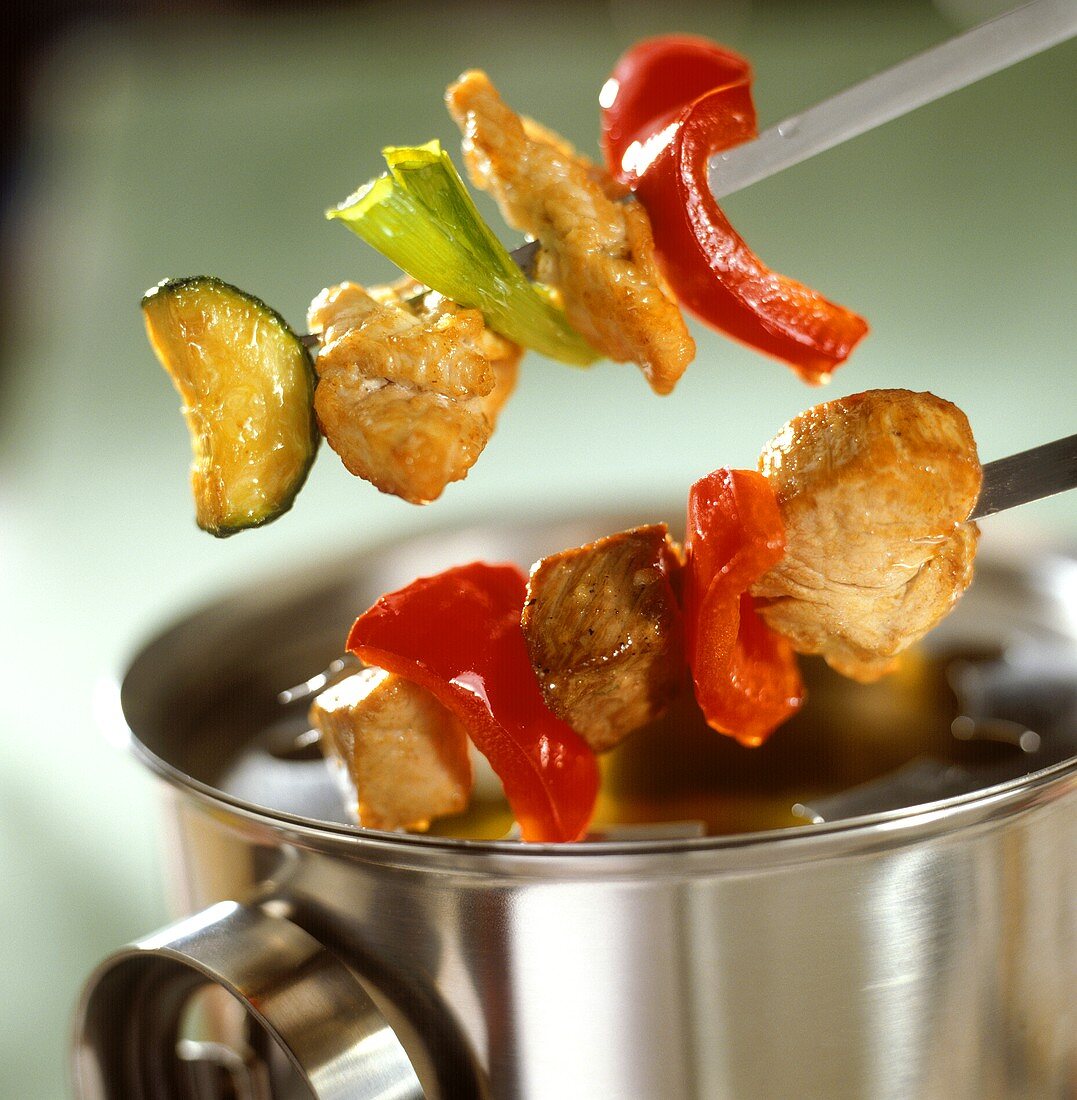 Meat fondue kebabs above stainless steel pot