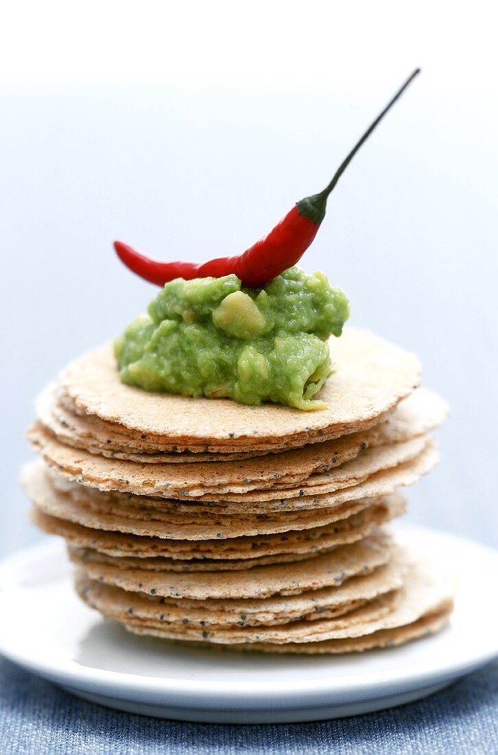 Avocado dip with chili pepper on poppy seed crackers