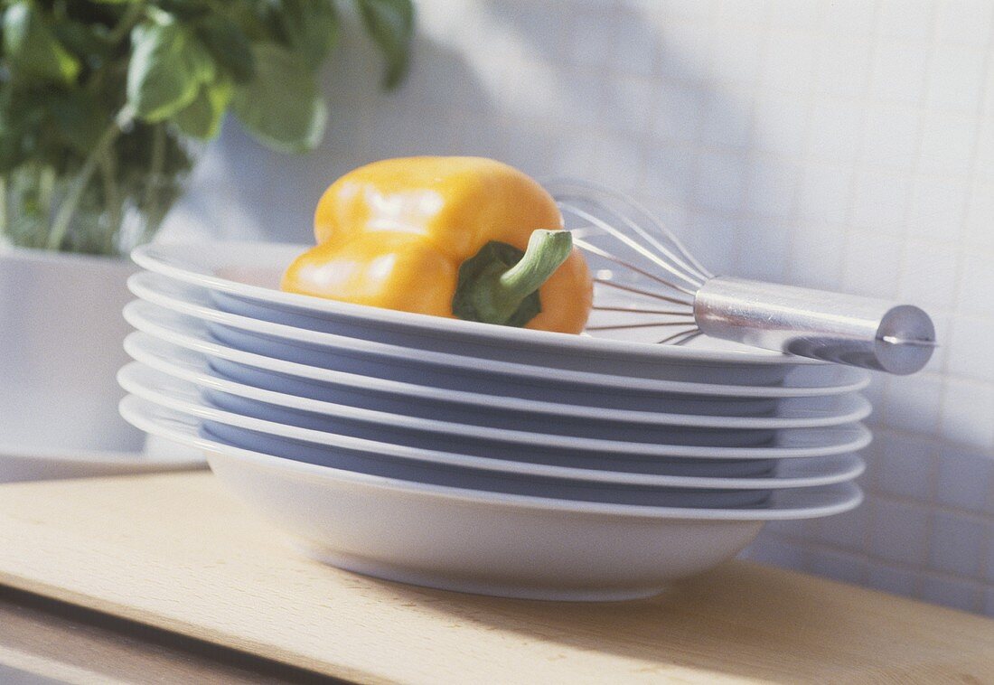 Yellow pepper on pile of plates with egg whisk