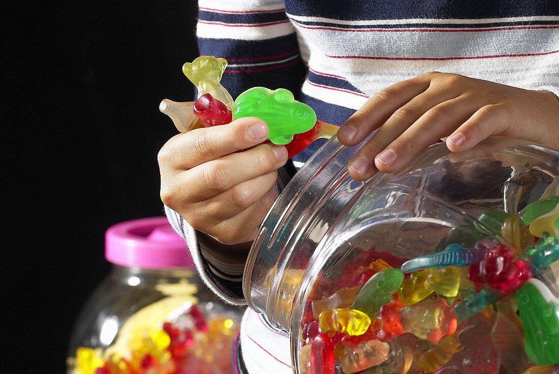 Children's hands holding coloured fruit gum with jar