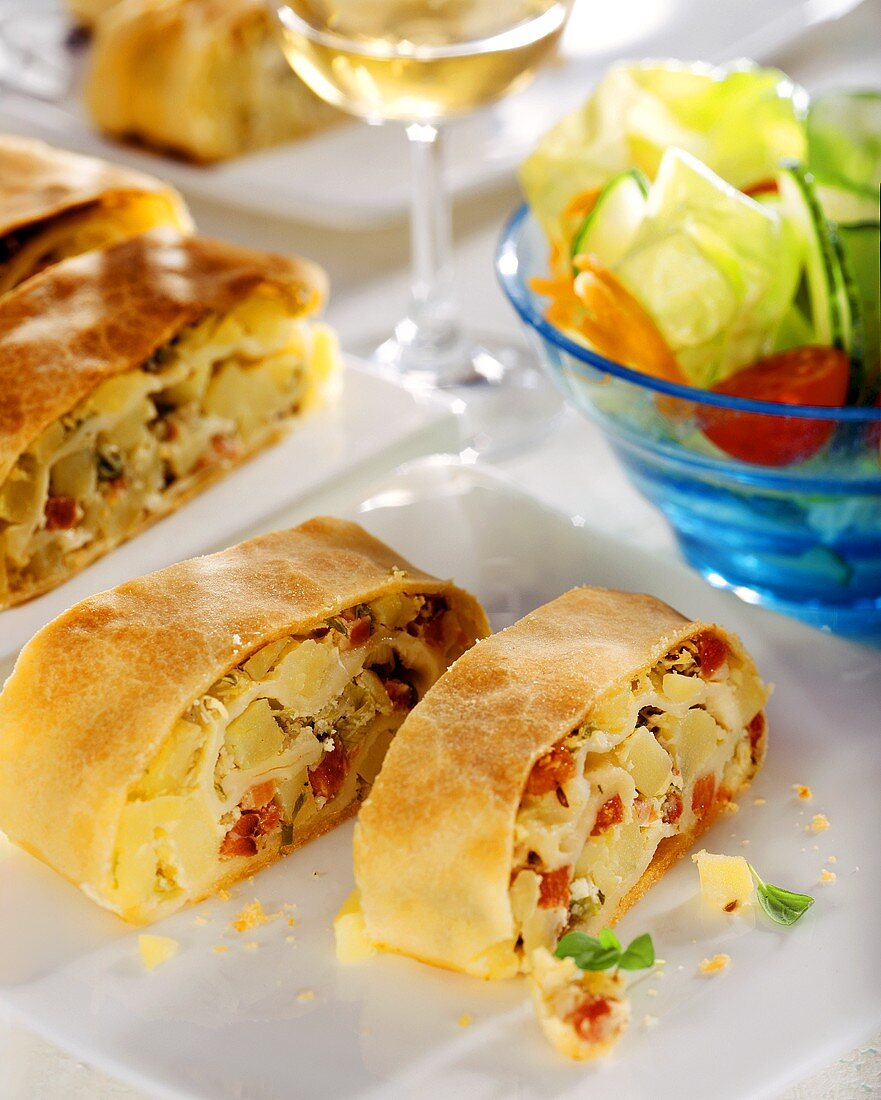 Potato strudel with bacon; salad; white wine glass