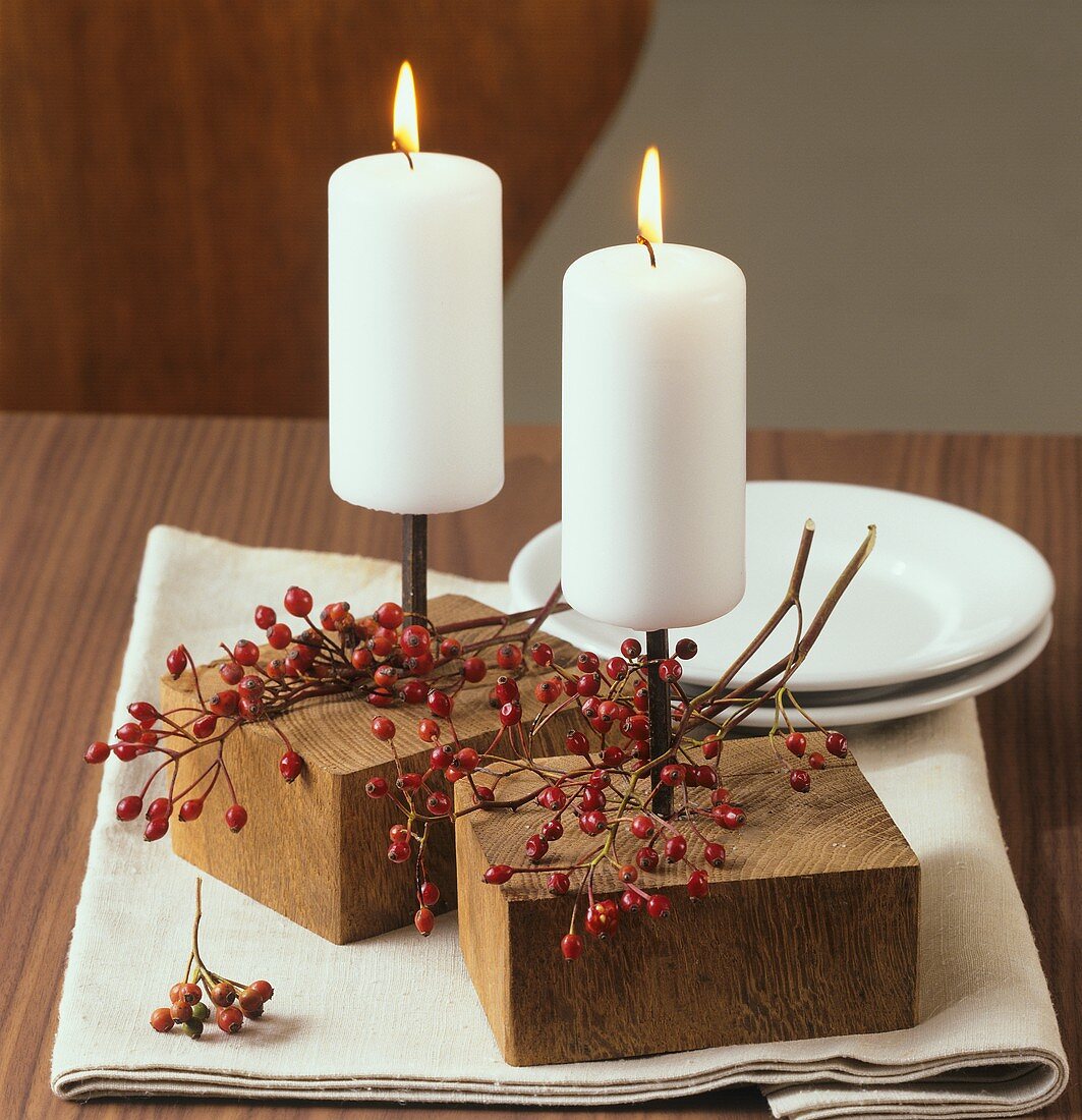 Table decoration: white candles and branch of rose hips