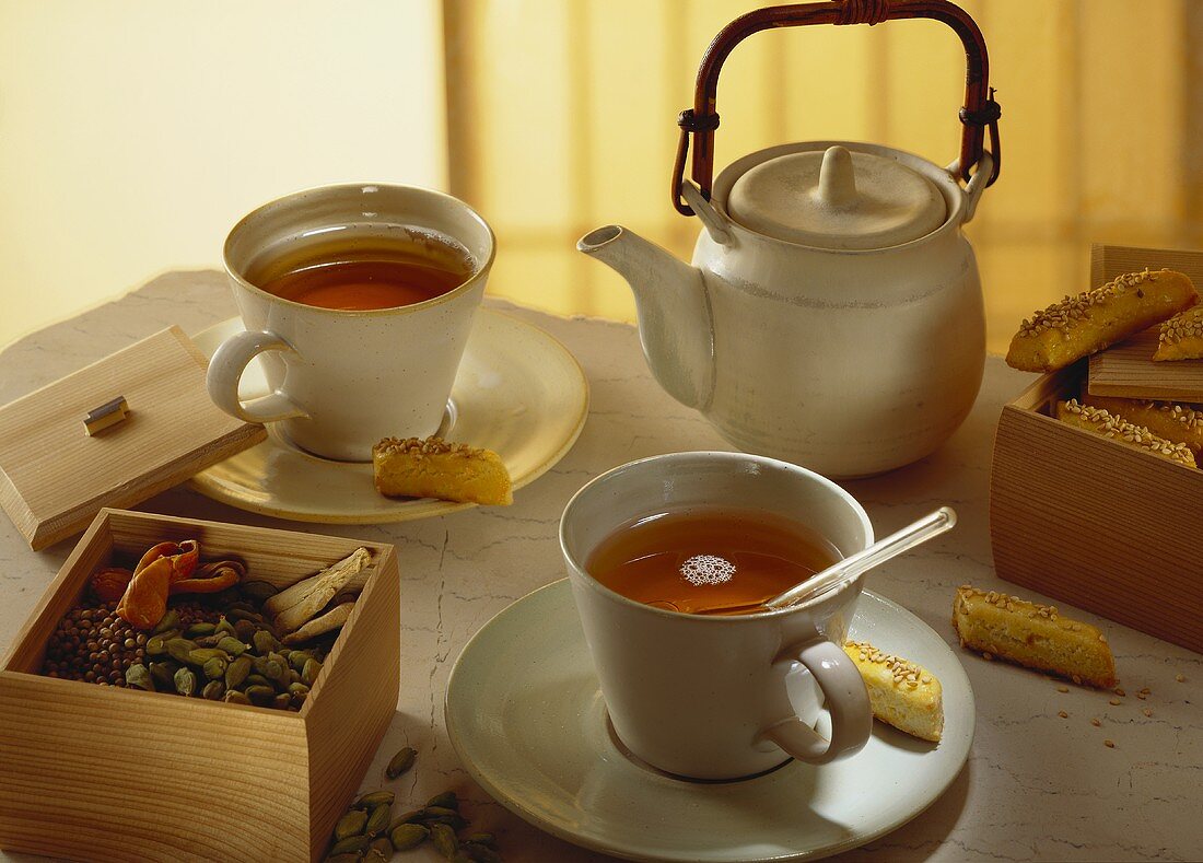 Schwarzer Tee in Tassen und Kanne; Gewürze; Sesamgebäck