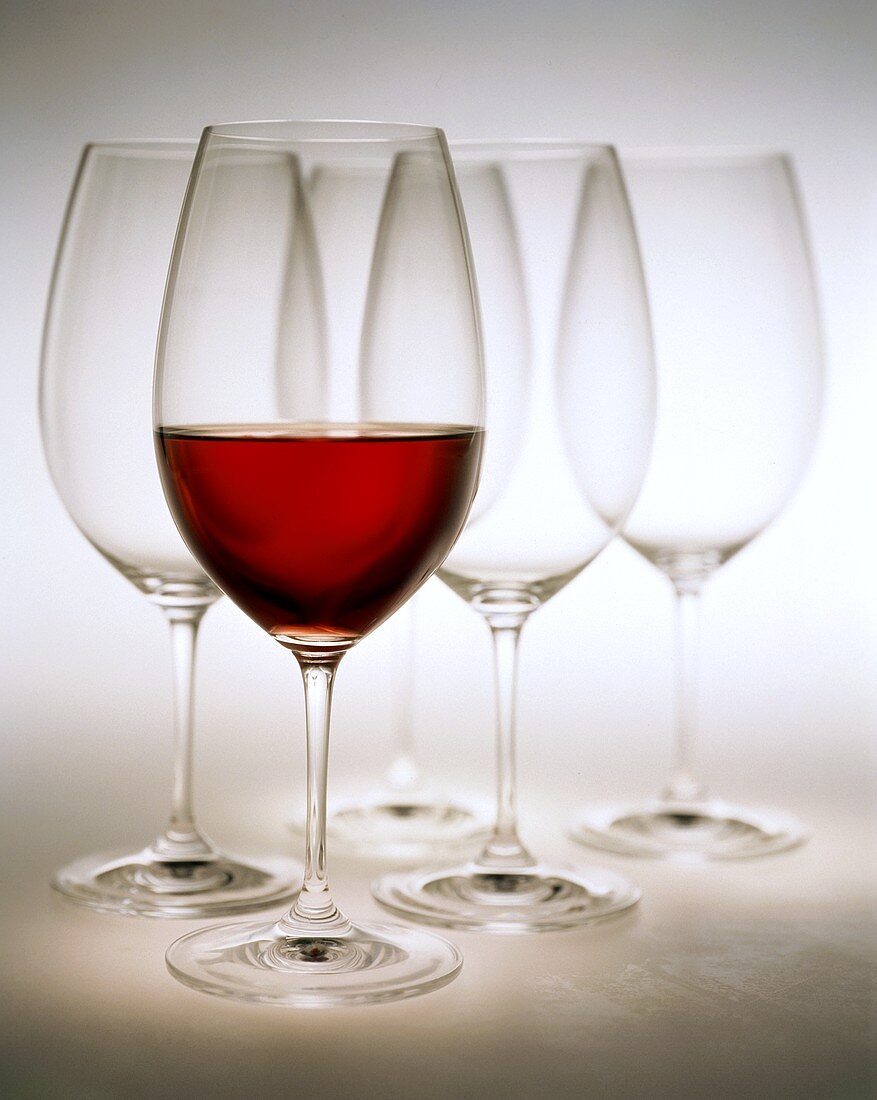 Glass of red wine in front of empty red wine glasses