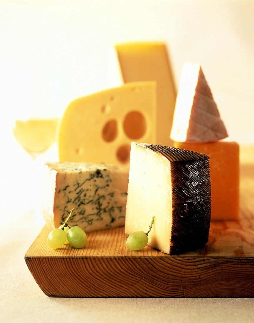 Various types of cheese on wooden board with grapes