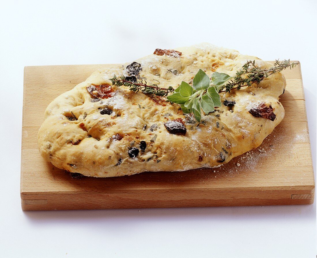 Focaccia with olives and dried tomatoes on wooden board