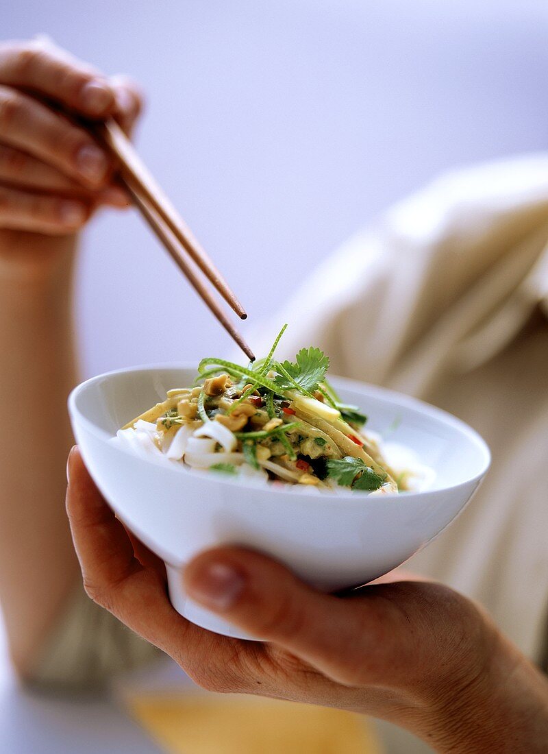 Person holding bowl of rice noodles with bamboo sprout sauce
