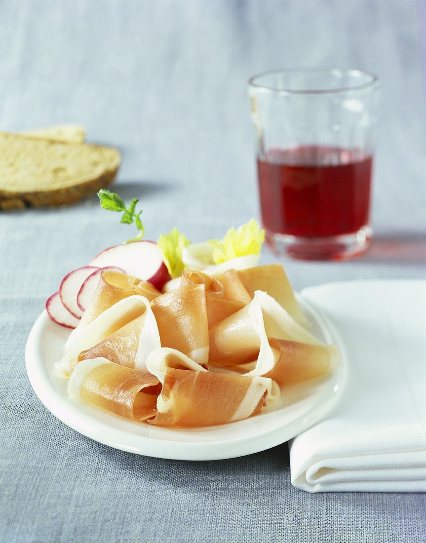 Schinkenspeck and radishes on plate; glass of red wine