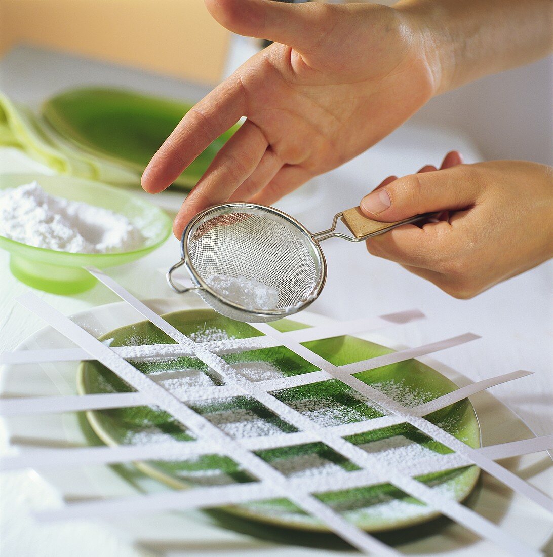 Hand sieving icing sugar on to plate with strips of paper