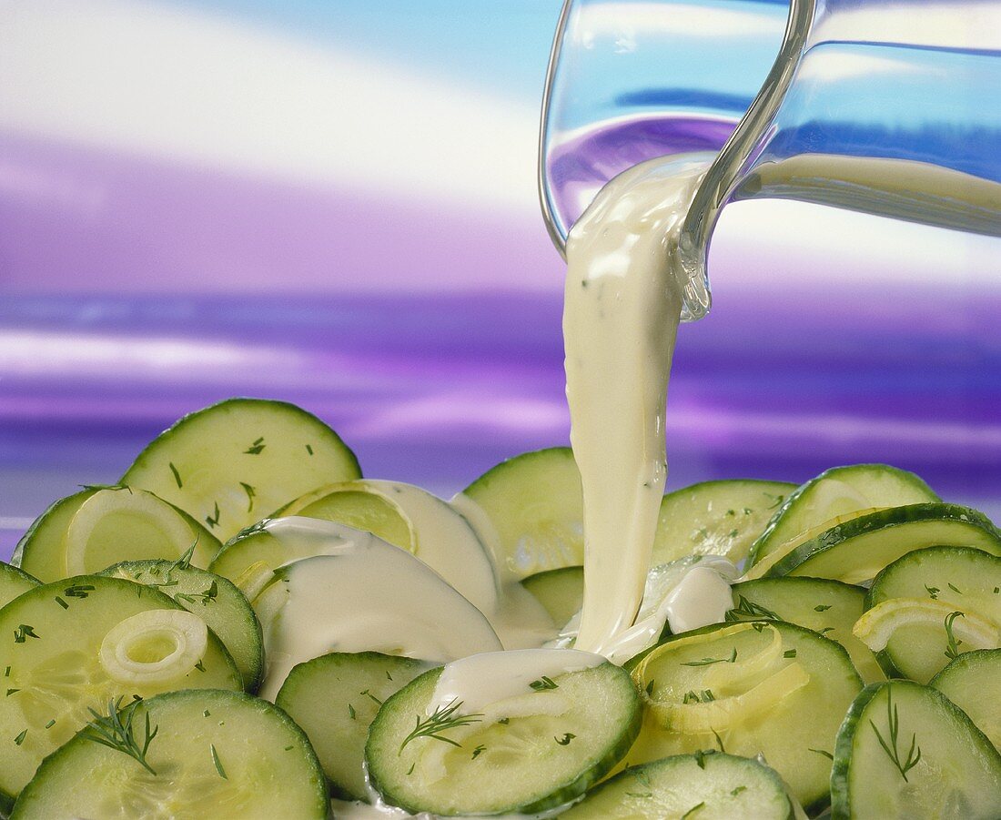 Pouring yoghurt dressing over cucumber salad