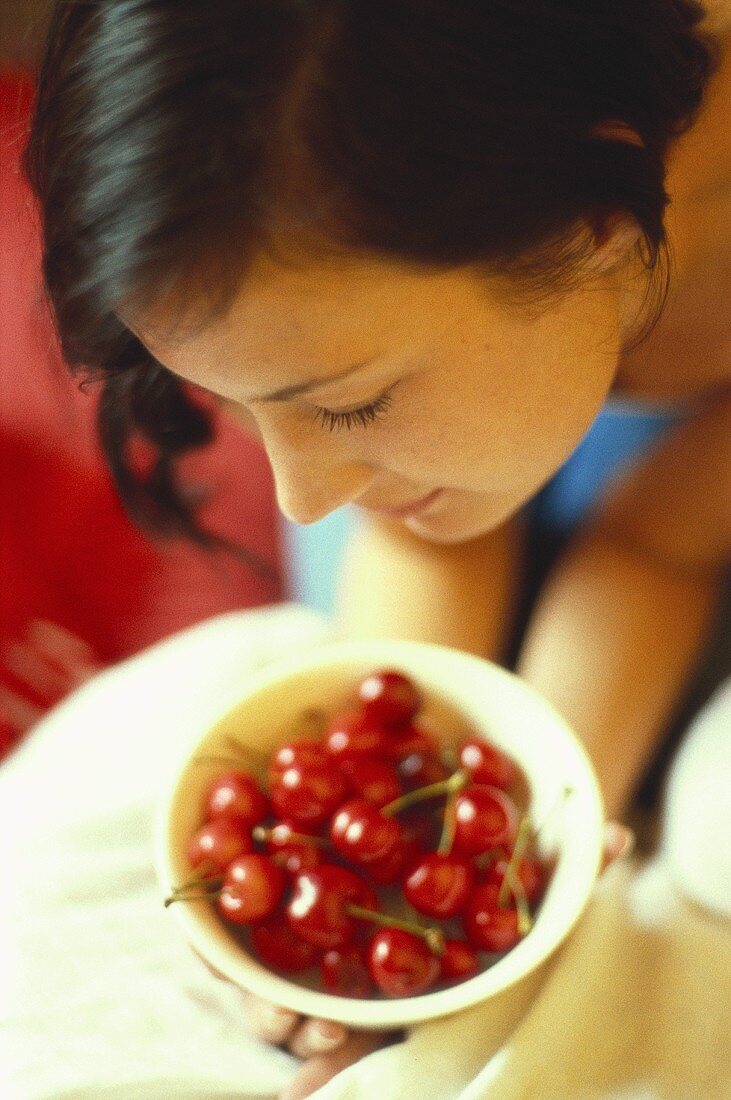 Young woman bending over bowl of red cherries
