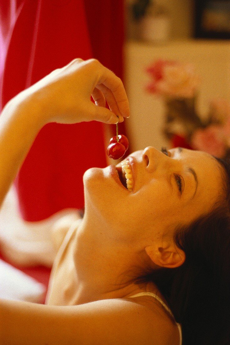 Laughing young woman eating a pair of cherries