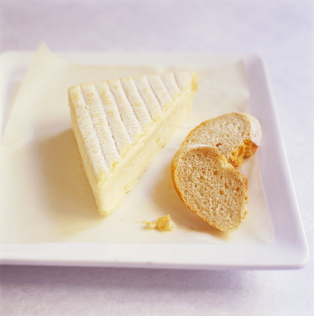 Piece of soft cheese with slices of bread on plate