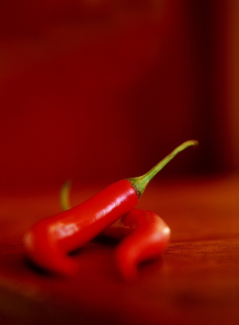 Two red chili peppers on wooden table
