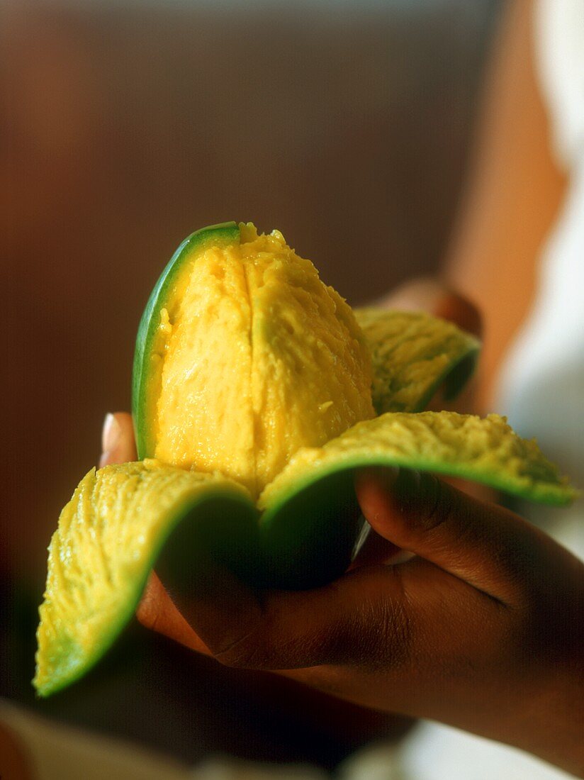 Hands holding half-peeled mango