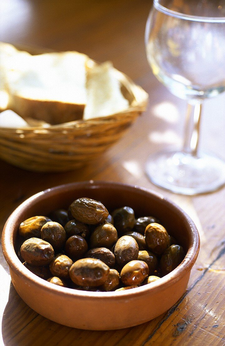 Eingelegte Oliven in Tonschale; Brotkorb; Weinglas