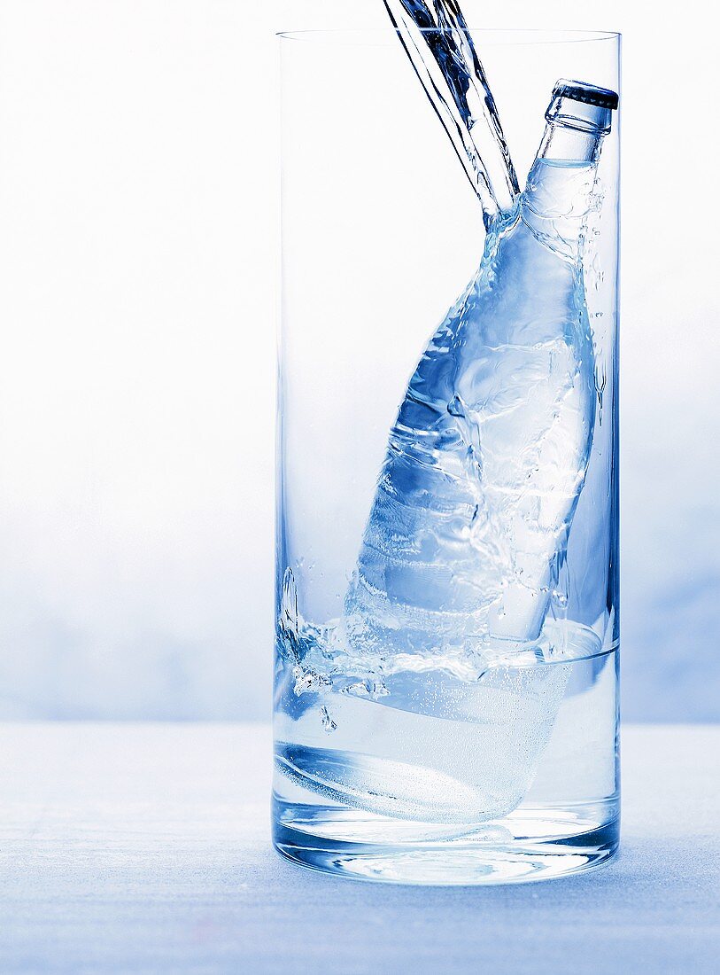 Wasserstrahl trifft Wasserflasche in Glasbehälter