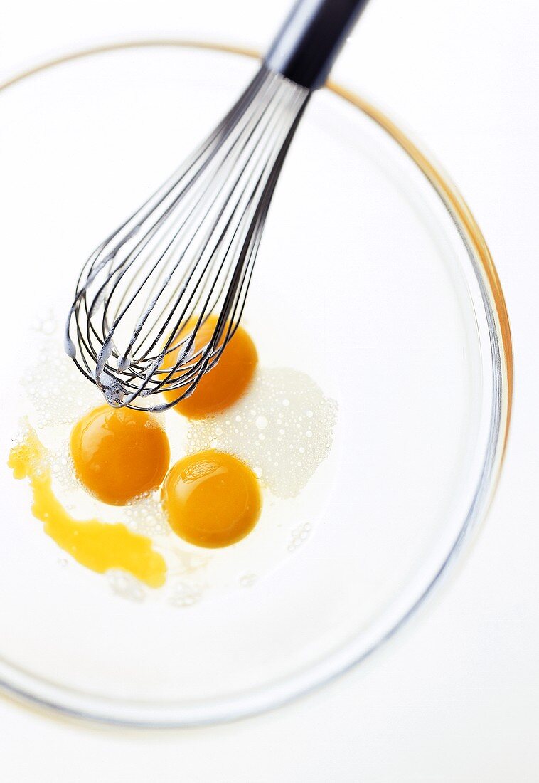 Three eggs broken into glass bowl, with whisk