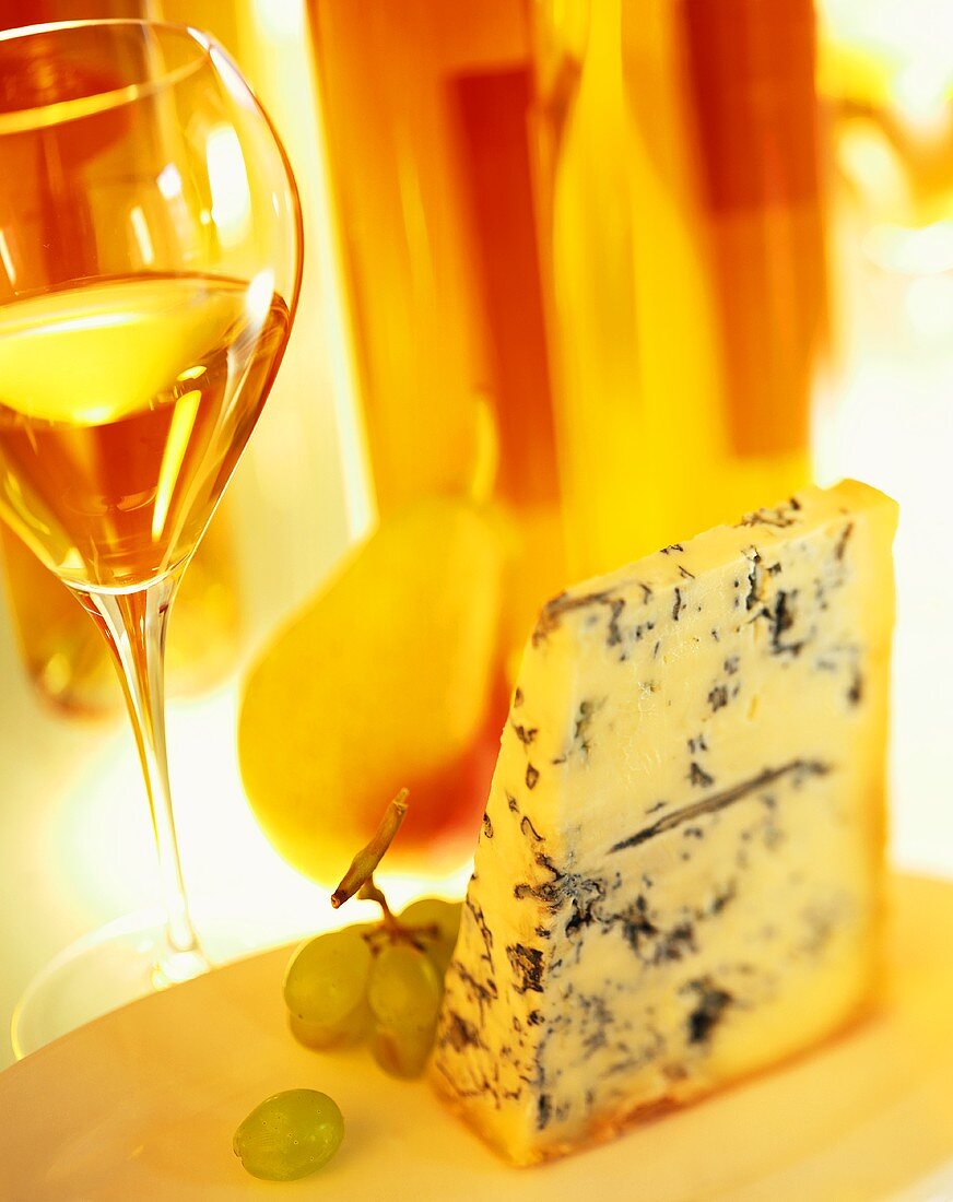 Piece of blue cheese with fruit and glass of white wine