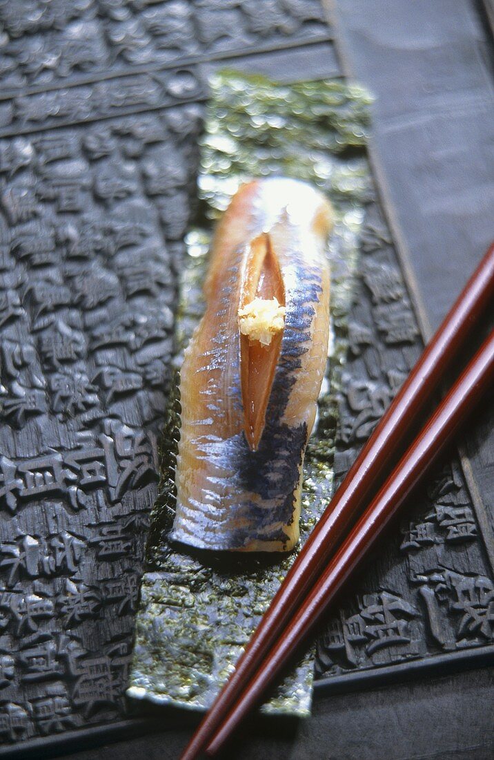 Ein Nigiri-Sushi mit Sardine, davor Stäbchen