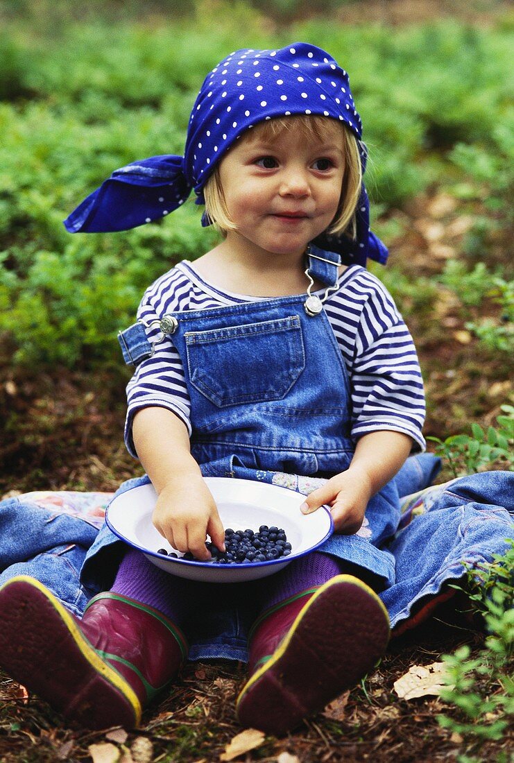 Kleines Mädchen mit Teller Heidelbeeren auf dem Feld