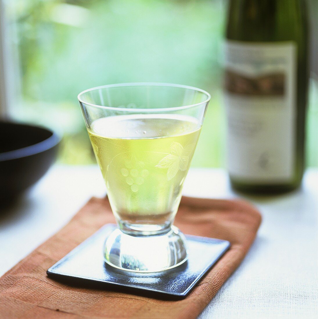 Glass of white wine on small tray in front of wine bottle