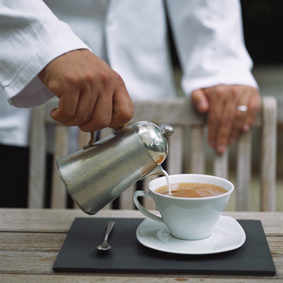 Kellner giesst Milch in Teetasse