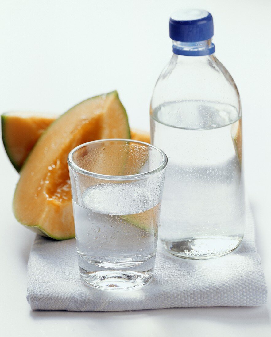 Water in glass and bottle in front of melon slices