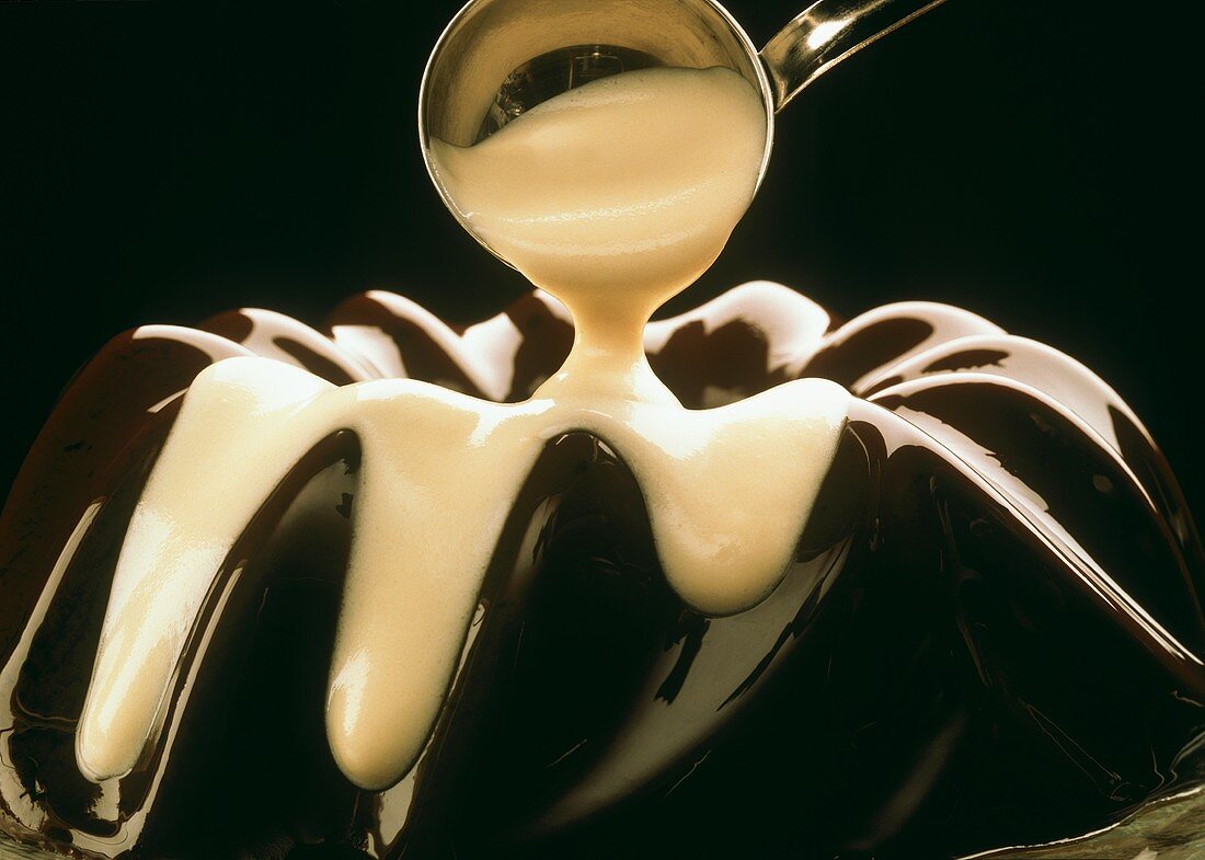 Pouring vanilla sauce over chocolate blancmange