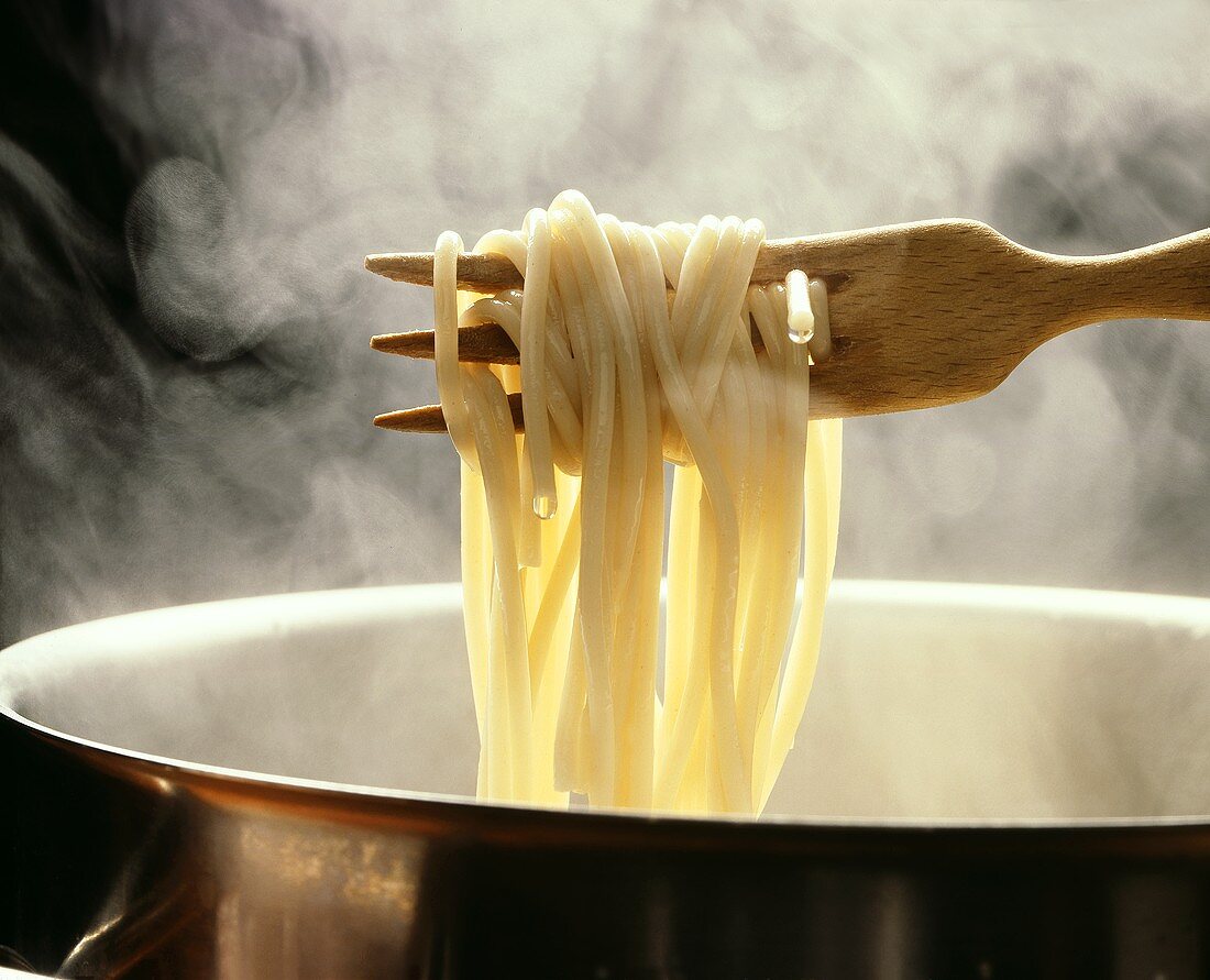 Lifting spaghetti out of a steaming pan with a wooden fork
