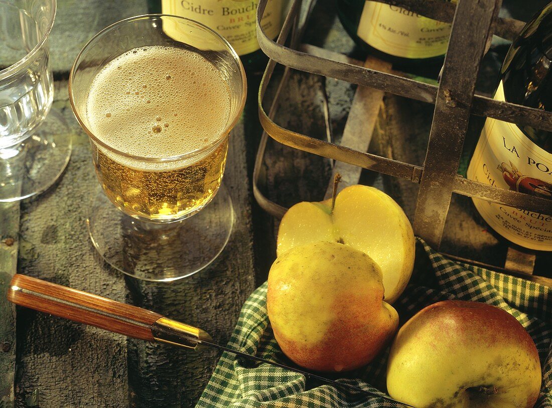 A glass of cider; apples and cider bottles