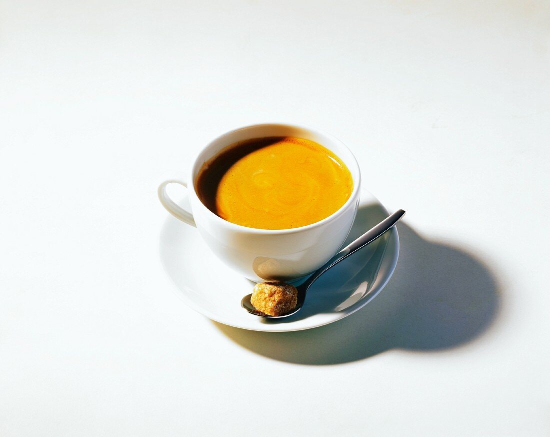 Eine Tasse Kaffee mit Löffel und einem braunen Zuckerwürfel