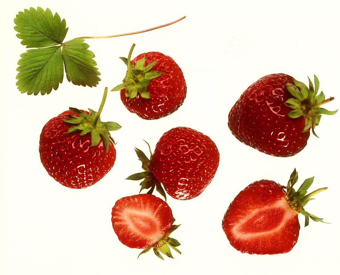 Whole and half strawberries and a strawberry leaf