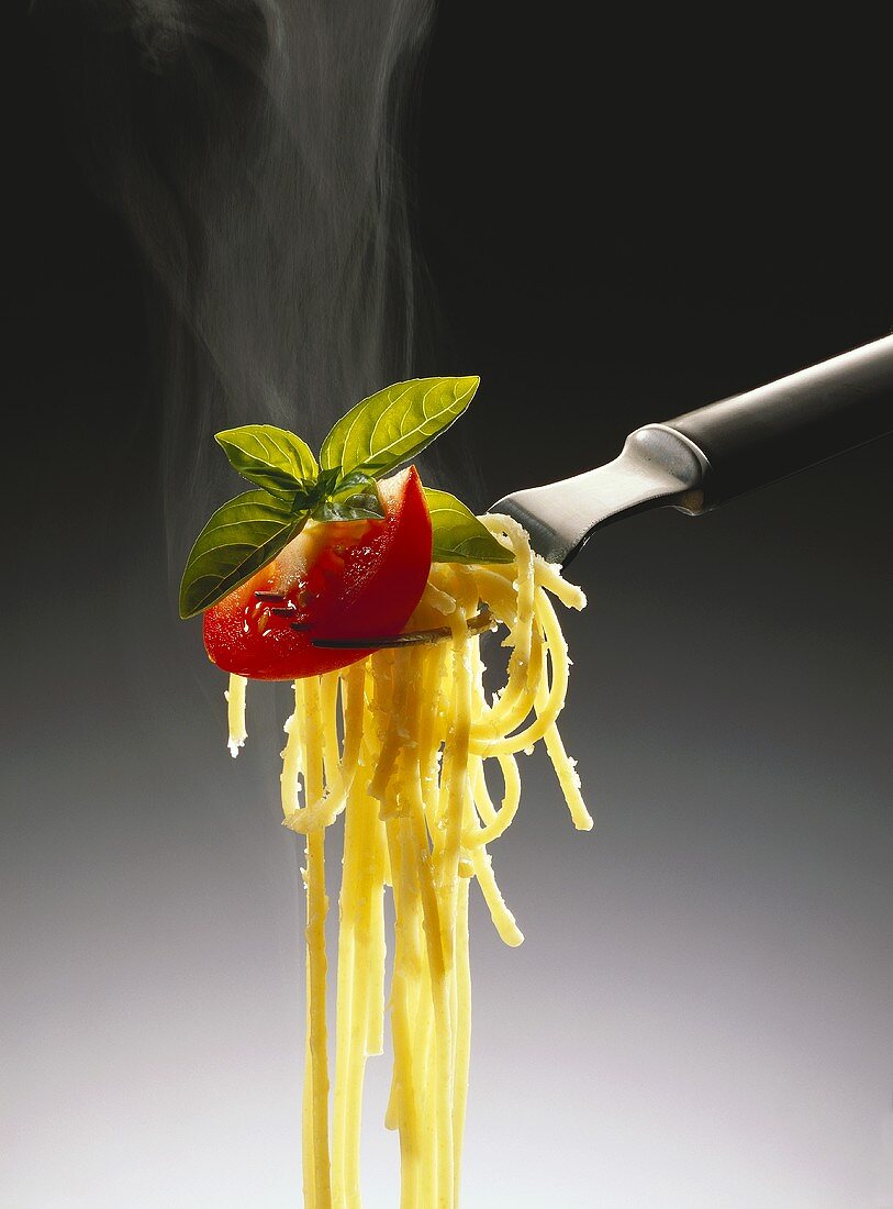 Spaghetti with cheese, tomato slice and basil on fork