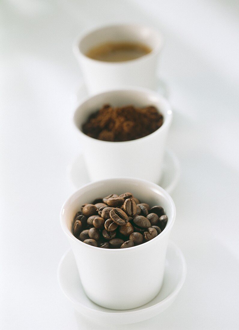 Kaffeebohnen, Kaffeepulver und Espresso in Schälchen
