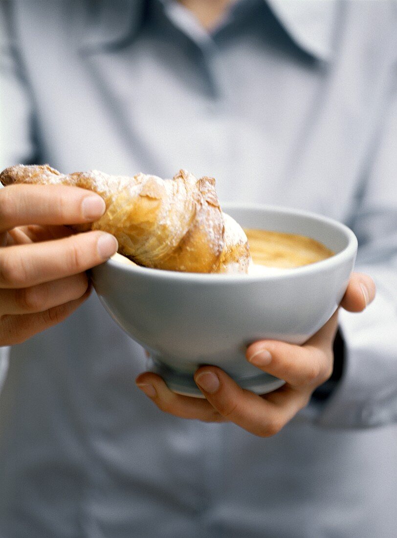 Hände halten Schälchen mit Milchkaffee und Croissant