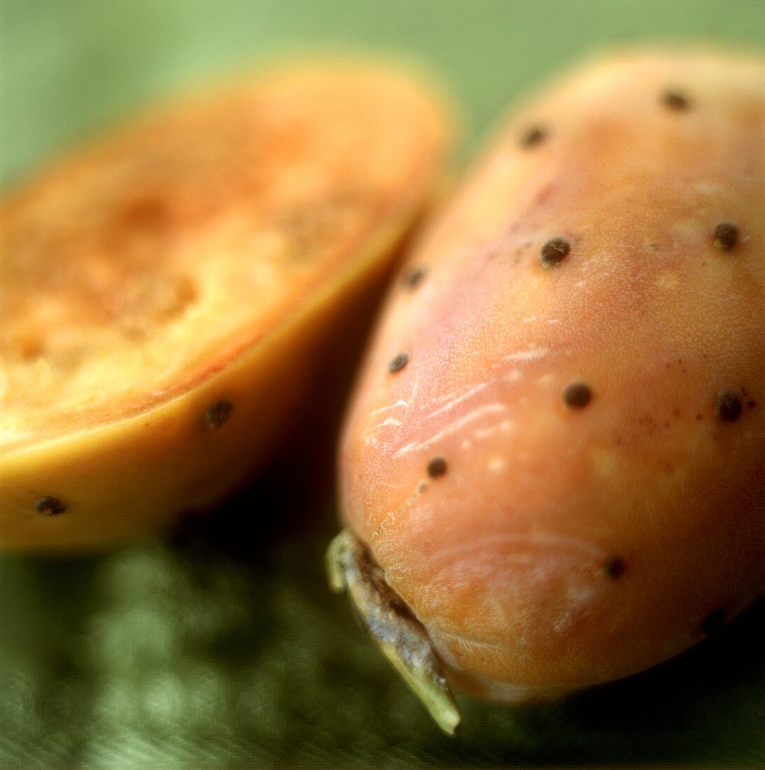 A whole and a half cactus fig on a green background